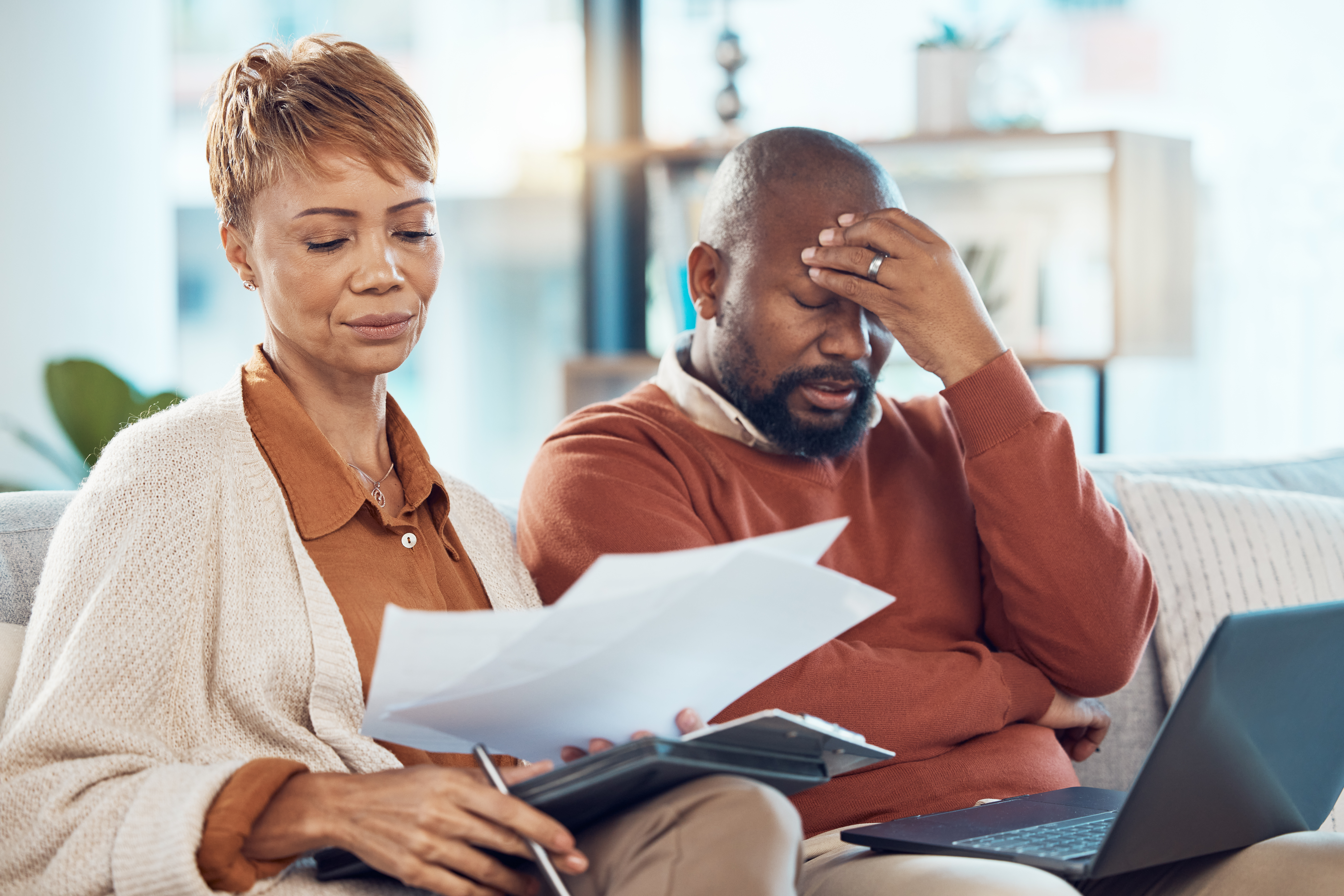 Black couple, stress and laptop in finance debt, expenses or dealing with financial exploitation together on the living room sofa at home.
