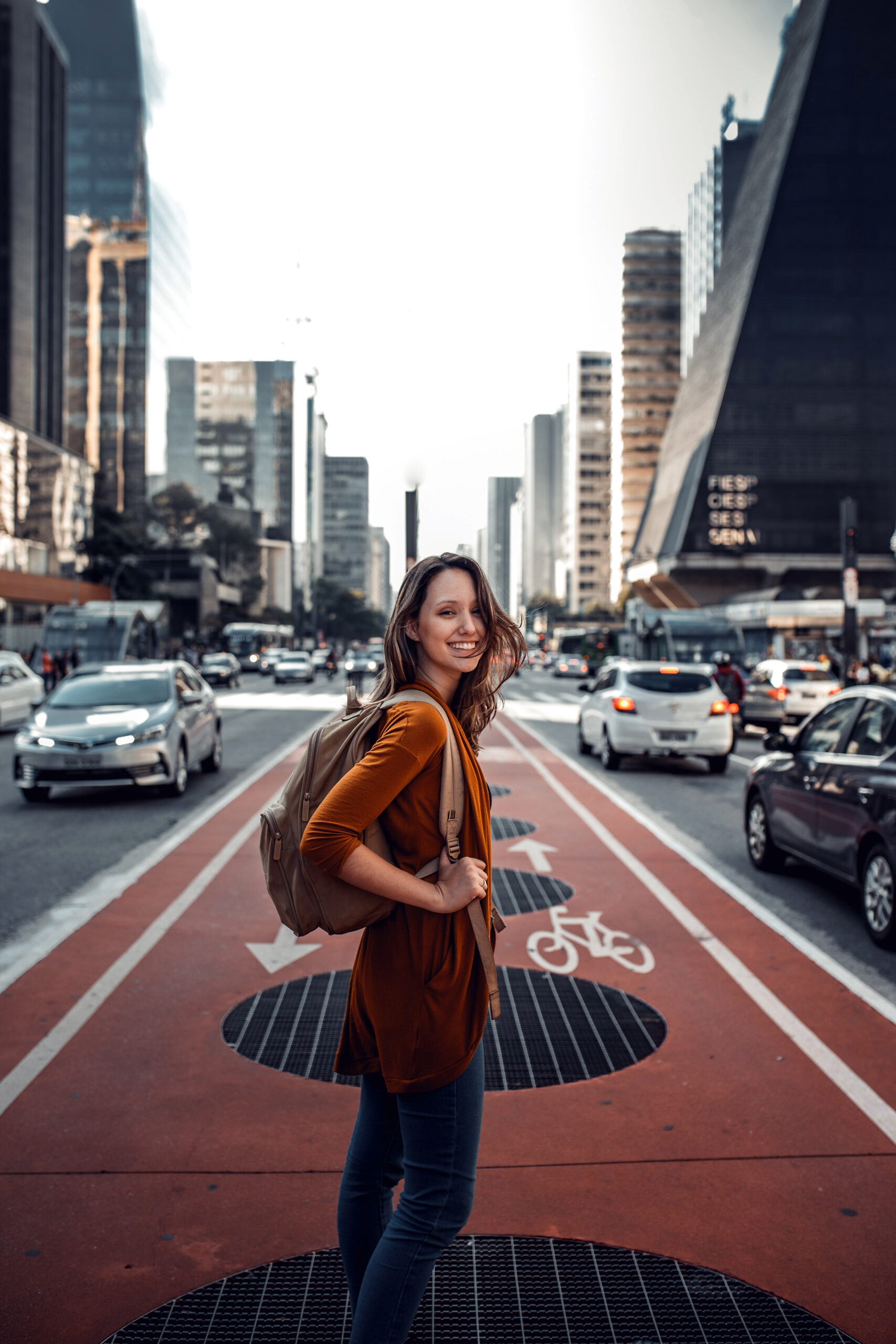 Woman standing in cross walk of busy street, while looking back and smiling