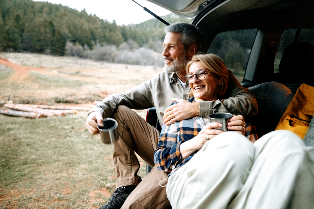 Middle aged couple sitting together in the back of an SUV, looking out at the mountains